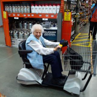 An elderly woman riding a mobility scooter in a store aisle.