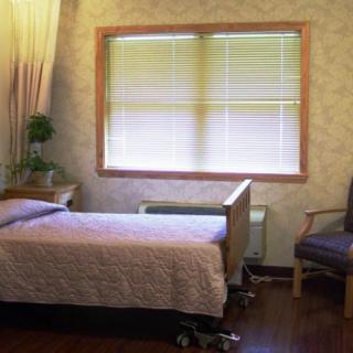 A simple hospital room with a bed, window, and chair.