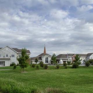 A suburban neighborhood with houses, a church, and a well-maintained lawn under a cloudy sky.