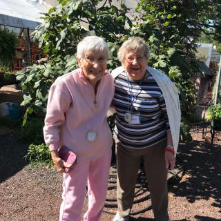 Two elderly individuals smiling together outdoors in a garden setting.