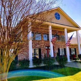 A two-story brick house with columns and American flags on a sunny day.