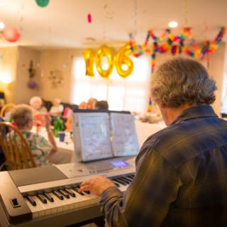 A lively birthday celebration with music being played on a piano, highlighting a milestone age of 106.