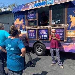 A group of people gather around a colorful food truck on a sunny day.