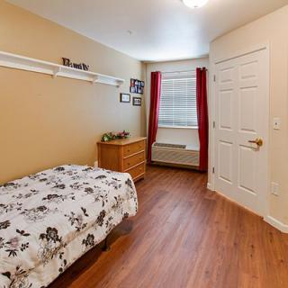 A cozy bedroom featuring a single bed with floral bedding, a wooden dresser, and bright red curtains by the window.