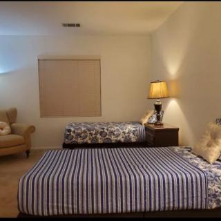 A cozy bedroom with two beds, a lamp on a nightstand, and an armchair.
