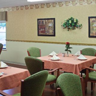 A cozy dining room with neatly set tables and comfortable green chairs, adorned with simple wall decorations and art.