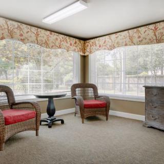 A cozy indoor seating area with two wicker chairs and a small round table by large windows.