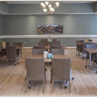 An empty dining room with neatly arranged tables and chairs, featuring a chandelier and wall artwork.