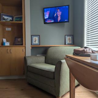 A cozy living room corner featuring a green armchair, wooden furniture, and a television mounted on the wall.