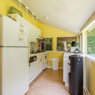 A bright kitchen with yellow walls and wooden flooring, featuring a refrigerator, cabinets, and ample natural light from large windows.
