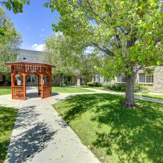 A sunny garden with a wooden gazebo and pathway surrounded by lush green trees.