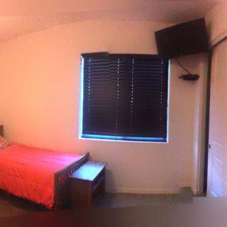 A minimalist bedroom with a single bed, closed blinds, and a wall-mounted TV.
