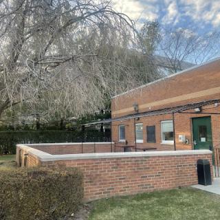 A view of a brick building surrounded by grass and trees under a cloudy sky.