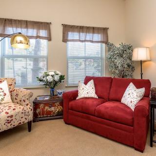 A cozy living room with a red sofa, floral chair, and ambient lighting.