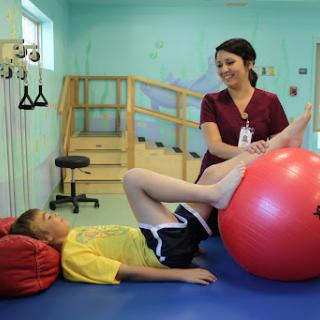 A therapist assisting a child with exercises using a therapy ball during a physical therapy session.