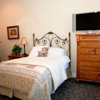 A cozy bedroom with a wrought iron bed, wooden furniture, and a mounted television.