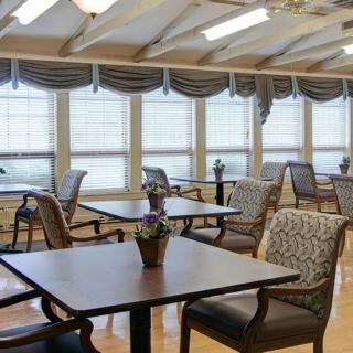 A well-lit dining area with tables and chairs, featuring large windows and elegant decor.