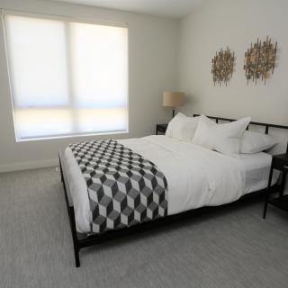 A modern and minimalist bedroom with a neatly made bed, geometric-patterned throw, and soft natural lighting.
