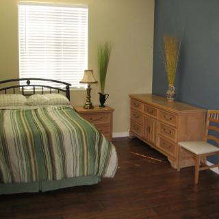 A cozy bedroom with a bed, dresser, lamp, and wooden flooring.