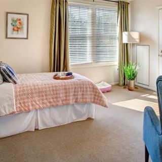 A cozy bedroom with natural light streaming through a large window, featuring a neatly made bed and tasteful decor.