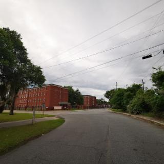 A peaceful urban scene featuring a winding road lined with trees and brick buildings under a cloudy sky.