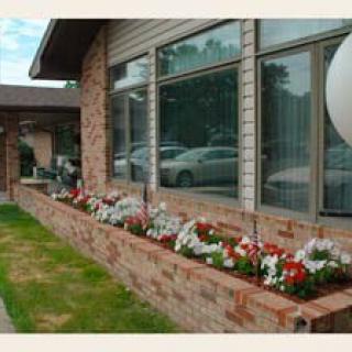 A brick building with large windows and a colorful flower bed in front.
