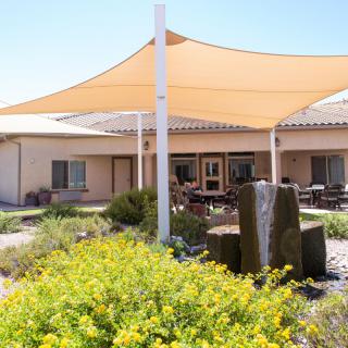 A peaceful outdoor patio area featuring a shade sail, fountain, and lush landscaping.
