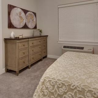 A cozy bedroom featuring a wooden dresser, elegant artwork, and a neatly made bed.