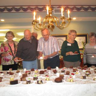 A lively gathering featuring a variety of desserts, where people enjoy the sweet treats under a beautiful chandelier.