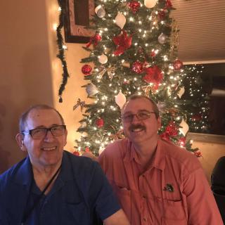 Two people smiling in front of a decorated Christmas tree.