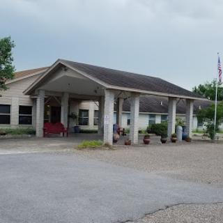 A welcoming entrance to a facility with landscaped surroundings and a flagpole.