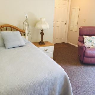 A cozy bedroom featuring a bed, nightstand with a lamp, and a cushy recliner chair.