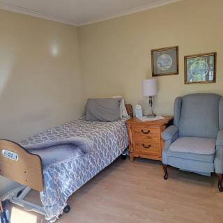 A cozy room featuring a hospital bed, an armchair, and a nightstand with a lamp.