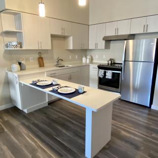 A modern kitchen with stainless steel appliances, featuring an open dining area and wood flooring.