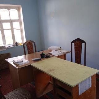 A simple office setup featuring a desk and chairs, illuminated by natural light from the window.