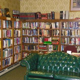 A cozy library corner with a green leather couch and rows of books on wooden shelves.