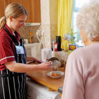 A caregiver preparing a meal for an elderly person in a kitchen setting.