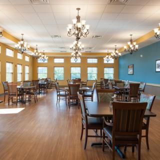 A spacious dining room featuring wooden tables and chairs, large windows, and elegant chandeliers.