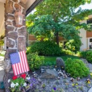 A garden scene featuring an American flag placed near a stone pillar surrounded by lush greenery and flowers.