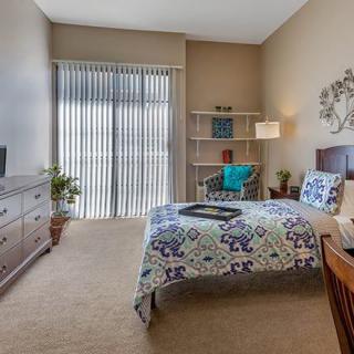 A cozy bedroom with a bed, dresser, and bookshelf under soft lighting.