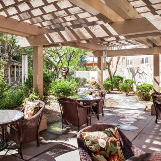 A cozy patio with comfortable seating under a pergola, surrounded by lush garden greenery.