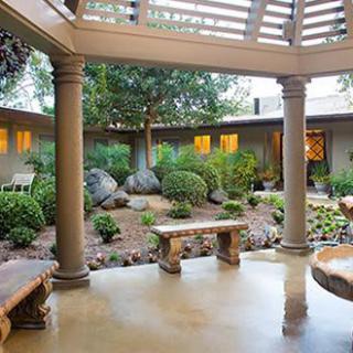 A beautifully landscaped courtyard with stone benches and columns, surrounded by greenery.