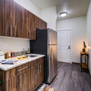 A modern apartment kitchen with wood cabinets and stainless steel appliances.