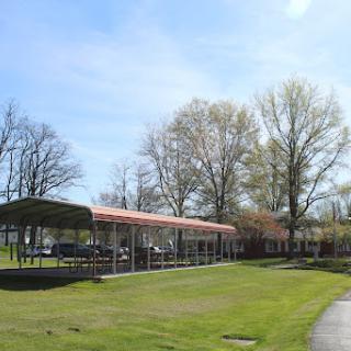 A sunny day at the park featuring a pavilion surrounded by trees and green grass.