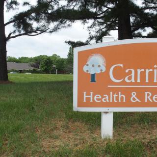 Sign for a health and rehabilitation facility set amidst trees and grass.