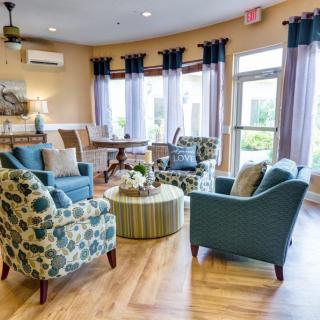 A cozy living room with multiple chairs, a small table, and large windows with curtains.
