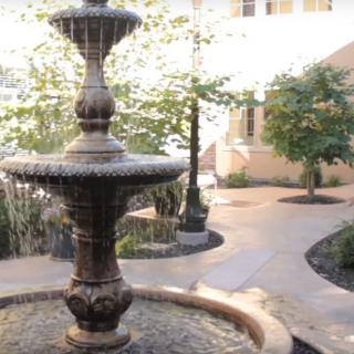 A tranquil courtyard featuring a two-tiered fountain surrounded by landscaped pathways and greenery.