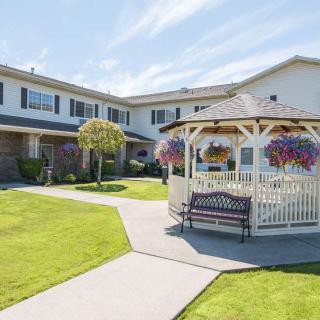 A well-maintained garden with a gazebo, surrounded by a two-story building and colorful flowers.