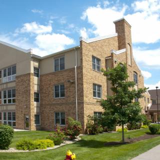 A brick residential building with a well-maintained lawn and trees under a partly cloudy sky.