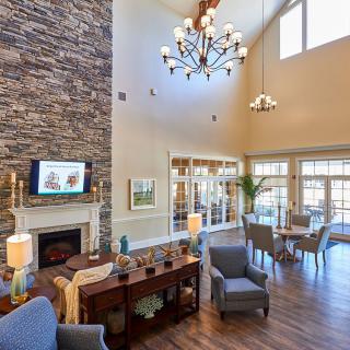 A spacious living room with modern decor, featuring a high ceiling, chandelier, stone fireplace, and comfortable seating.